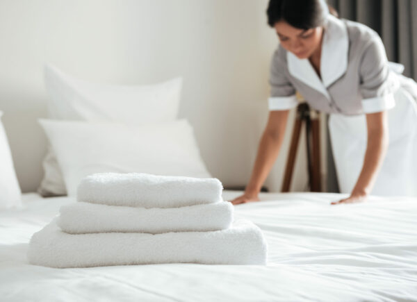 Young hotel maid setting up pillow on bed Young hotel maid making the bed with clean fresh towels